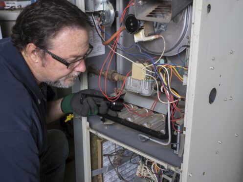 Technician looking over a gas furnace with a flashlight before cleaning it.